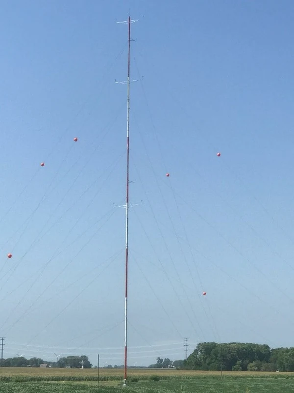 Red and white guyed meteorological mast installed in an open field