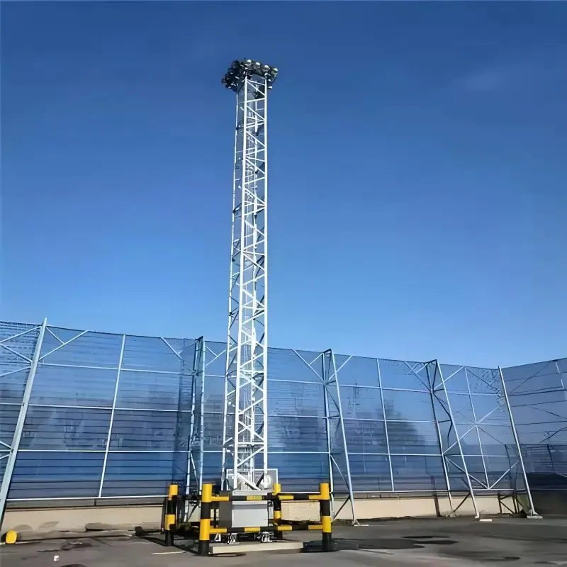 High mast lighting tower on a steel base beside a wind fence