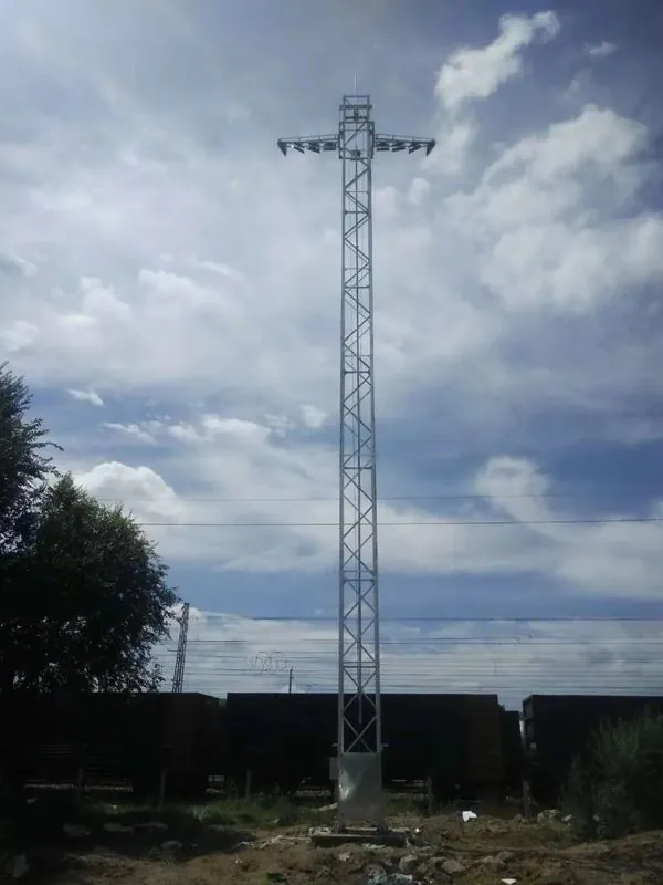 Galvanized floodlight tower with cross-arm lights above a rail yard