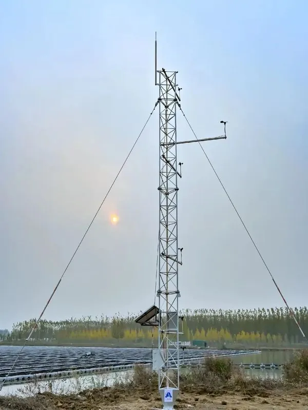 Guyed wind measurement tower with anemometer booms, solar panel and data cabinet