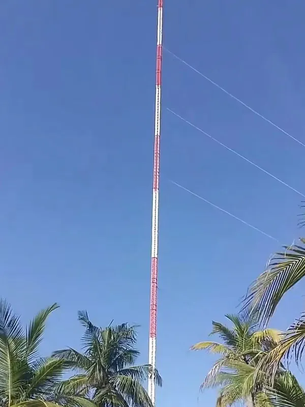 Red and white guyed tubular wind measurement mast installed at a coastal site