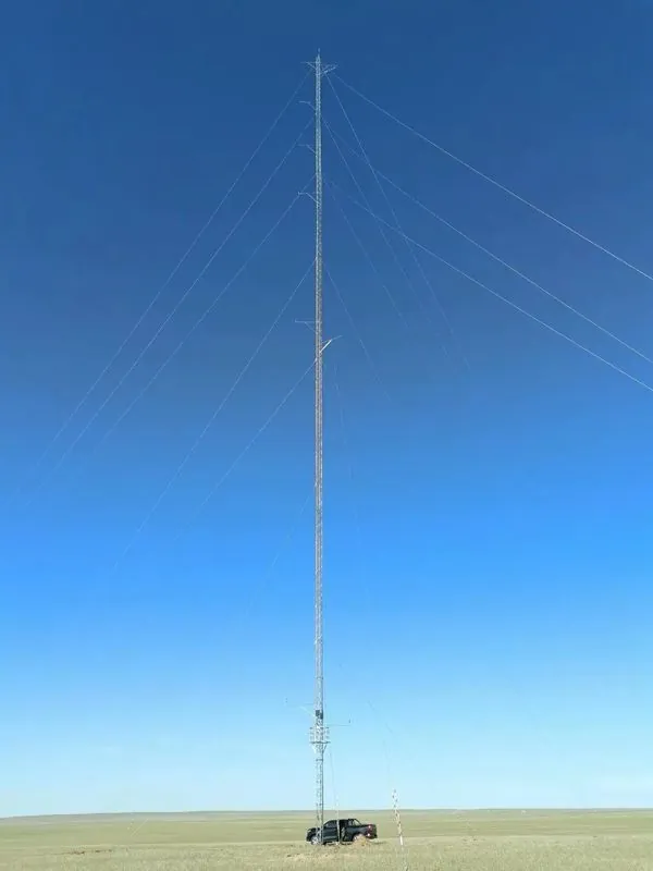 Guyed wind measurement tower installed on open grassland with a close view of the mast top